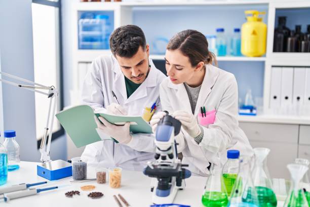istock Man and woman wearing scientist uniform using microscope writing on notebook at laboratory 1404480617