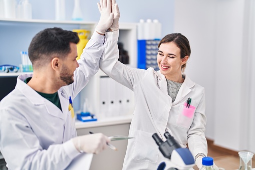 Man and woman wearing scientist uniform high five with hands raised up at laboratory
