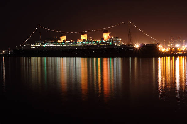 Long Beach, California - January 11, 2025: Queen Mary, a historic ocean liner converted into a hotel and museum, is docked in Long Beach, California, with golden sunset lighting illuminating the scene.