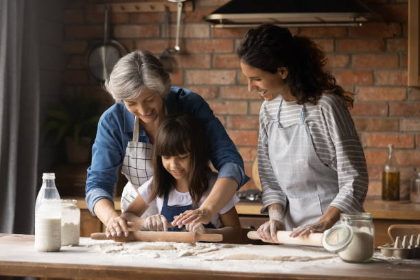 glückliche hispanische mutter und oma, die mädchen das backen beibringt - grandmother cooking baking family stock-fotos und bilder