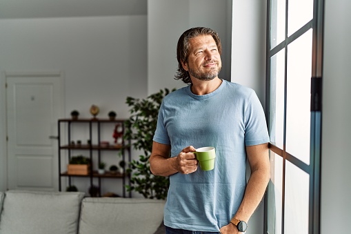 Hombre caucásico de mediana edad sonriendo confiado bebiendo café en casa photo