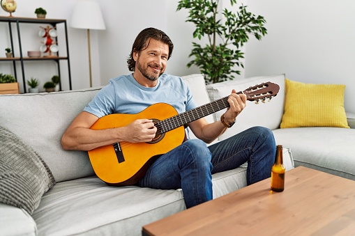 Middle age caucasian man smiling confident playing classical guitar at home