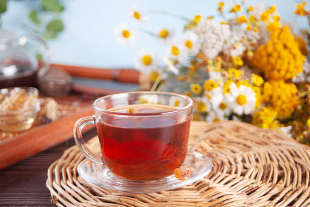 Cup of herbal tea with flowers, honey in jar, teapot and and various dried herbs on the tray. stock photo