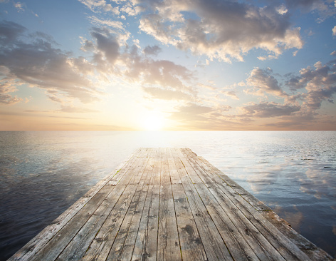 Long pier leading out into the lake, sunrise, sky and clouds on lake