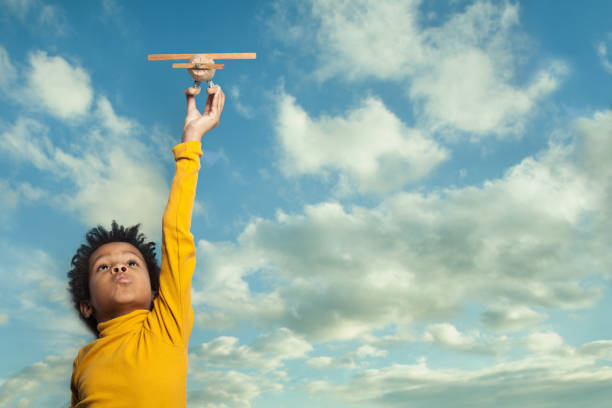 curioso niño negro con avión contra nubes azules del cielo de fondo - inventor fotografías e imágenes de stock