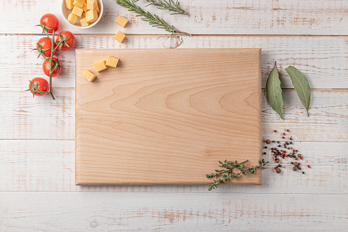 square wooden cutting board with cherry tomatoes, cheese and spices on a white background. mockup with copy space for text, top view