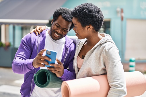African american man and woman couple holding yoga mat using smartphone at street