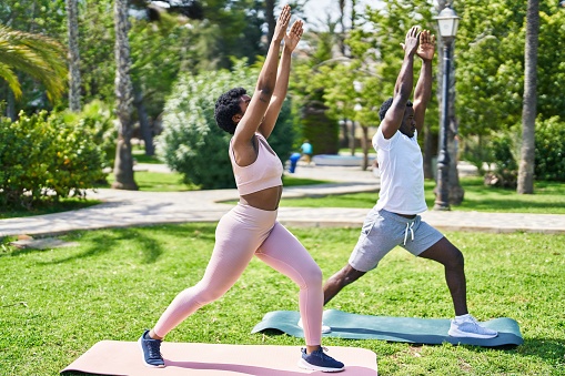 African american man and woman couple doing yoga exercise at park