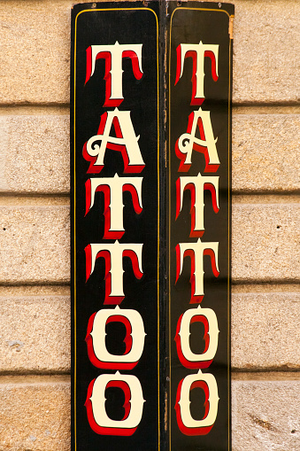 Close-up view of retro style Tattoo studio sign in old town Santiago de Compostela, Galicia, Spain. Stone building facade in the sunlight.