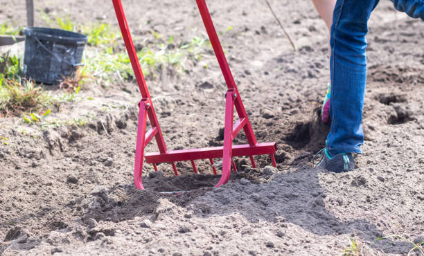 istock A farmer in jeans digs the ground with a red fork-shaped shovel. A miracle shovel, a handy tool. Manual cultivator. The cultivator is an efficient hand tool for tillage. Loosening the bed. 1404488264