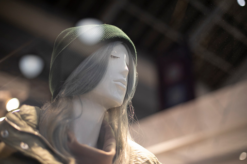 Mannequin of clothing. Girl in hat. Plastic figure of person. Details of shop window in clothes. Face of girl with long hair.