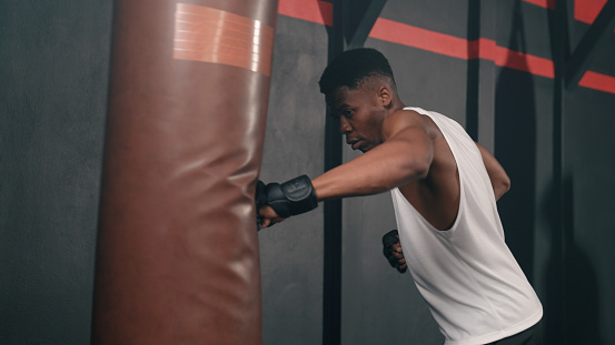 A young African man punching a punching bag while he's on a boxing session.