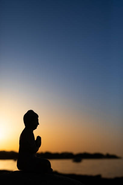 Praying Buddha silhouette on real sunrise. Strong backlighting and possible noise. For zen, mindfulness and other spiritual concepts.