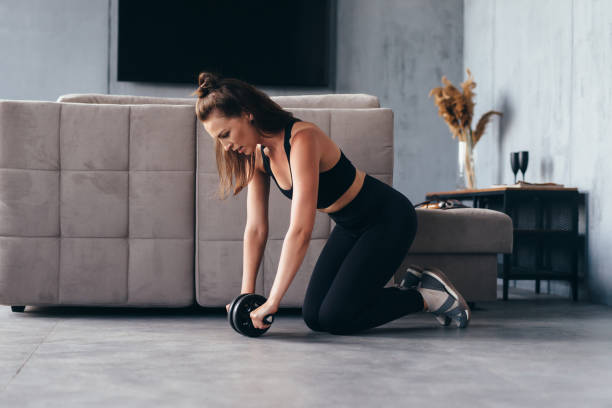 istock Fit woman working out with ab exercise wheel at home. 1404494100