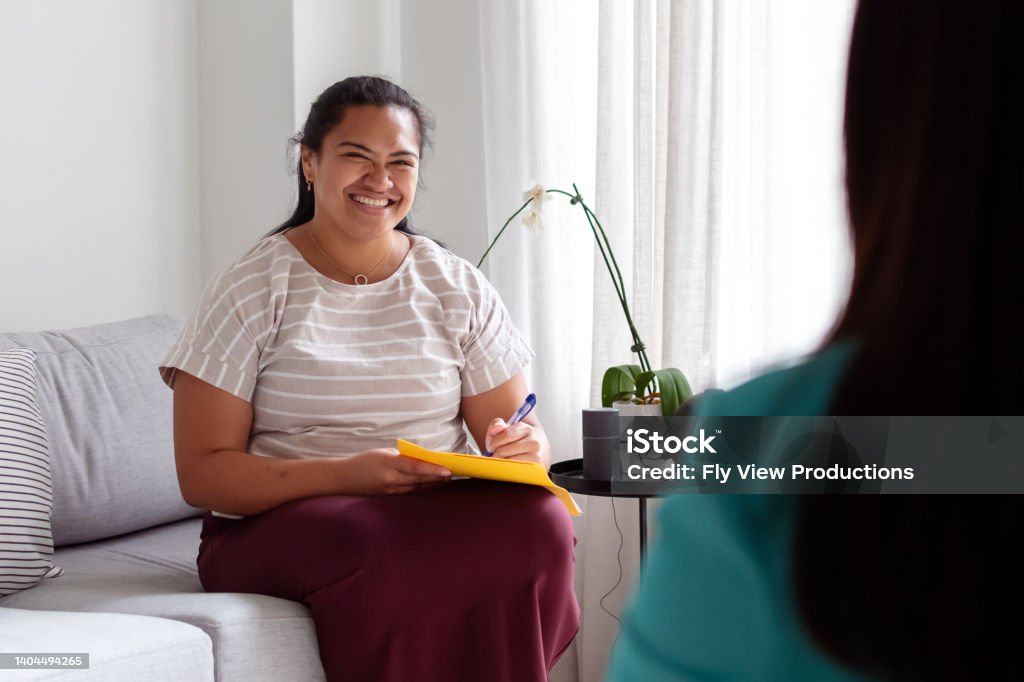 Encouraging therapist talking with female patient A positive young therapist of Pacific Islander descent smiles while talking with an unidentifiable female client during a psychotherapy session. Mental Health Professional Stock Photo