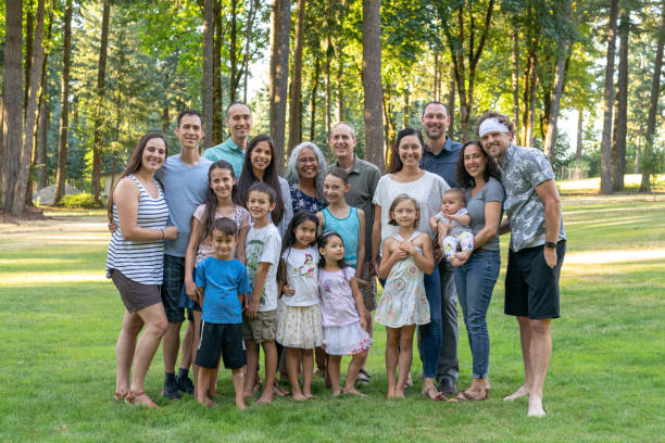 Multi-generation family celebrating reunion together outdoors Portrait of a senior couple posing for a photograph with their adult children and grandchildren. The multi-ethnic and multi-generation group is gathered at a family reunion. The family members affectionately have their arms around one another and are smiling. They are standing in a grassy meadow with trees in the background. 6 11 months stock pictures, royalty-free photos & images