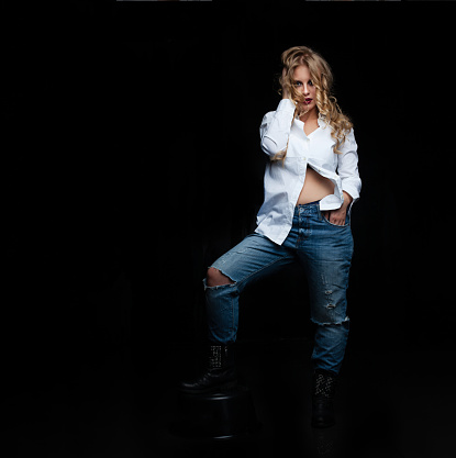 Attractive woman with blond hair in denim jeans on black background