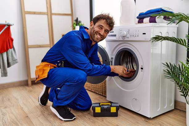 Young hispanic man wearing handyman uniform repairing washing machine at laundry room stock photo