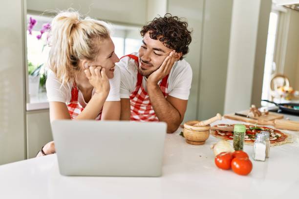 istock Young couple smiling happy using laptop at kitchen. 1404499846
