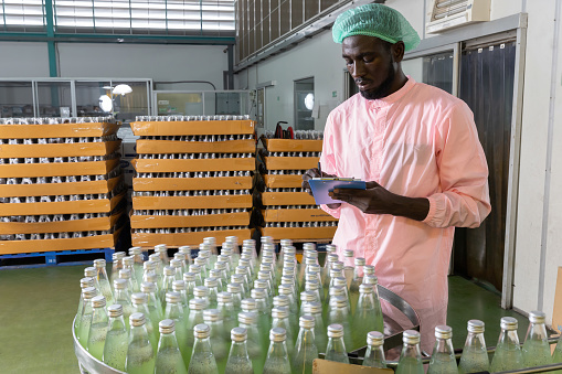 African male factory worker writing on clipboard looking and checking for stocktaking of products in beverage factory