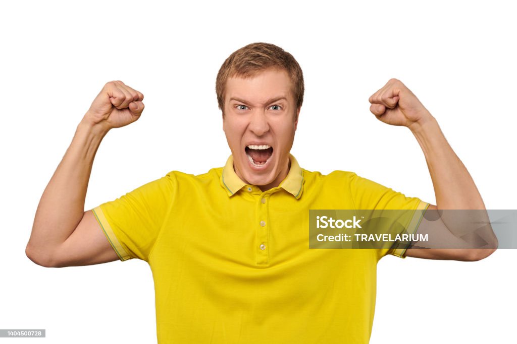 Funny young man in casual yellow T-shirt raising hands and rejoicing of success, isolated background Funny young guy in casual yellow T-shirt raising hands and rejoicing of success isolated on white background. Excited crazy man showing muscles and shouting, joyful facial expression B117 - COVID-19 Variant Stock Photo