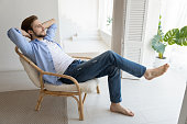 Untroubled millennial single man relaxing on chair in fashionable home