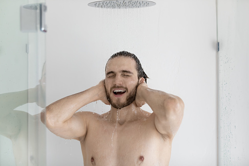 Man taking a shower rinse off shampoo and douche gel, standing under falling water in modern home or hotel bathroom, quality skincare and body care products, personal hygiene, morning routine concept