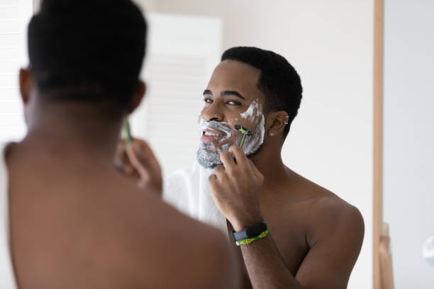 istock African guy looking in mirror shaving his face with razor 1404502159