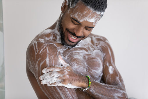 Close up cropped view young African man lather his muscular build body with hydrating shower gel, use natural quality fragrant bodycare wash product. Self hygiene, skincare, morning routine concept