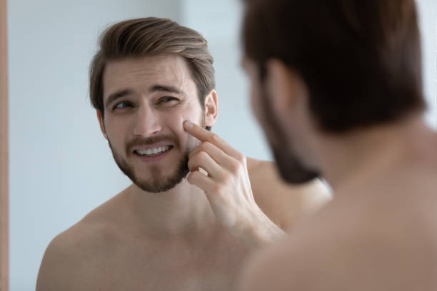 istock Man looking in mirror touch face with pimple on cheekbone 1404502475