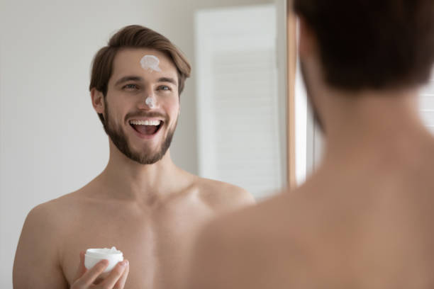 istock Handsome man with moisturizer cream on face looking in mirror 1404502478