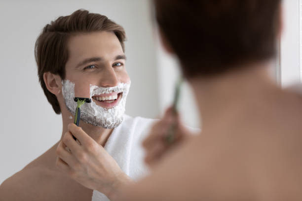 istock Handsome young man shaving his face and looking in mirror 1404502546