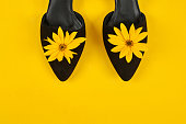 Suede black court shoes with yellow Topinambur flower bud on yellow background, womanhood concept