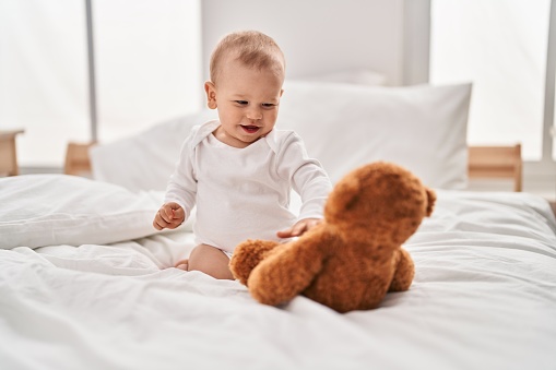 Adorable toddler playing with teddy bear sitting on bed at bedroom