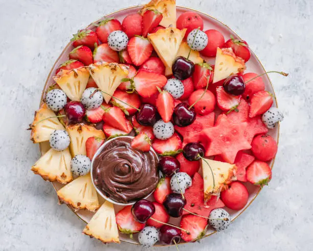 Overhead view of a large summer fruit platter with a small bowl of chocolate dip