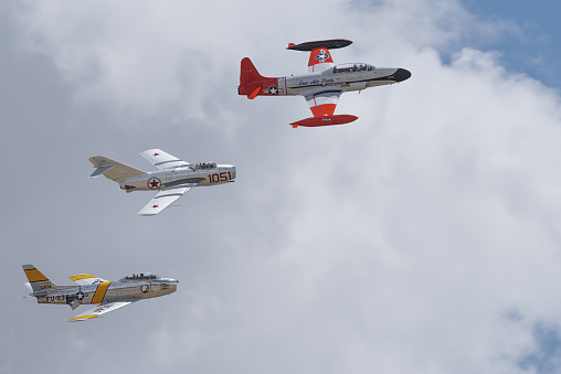 Chino, California, USA - May 7, 2017: Lockheed T-33 Shooting Star, Mikoyan-Gurevich Mig-15, and North American F-86F Sabre 'Jolley Roger' shown in flight against a cloudy sky..