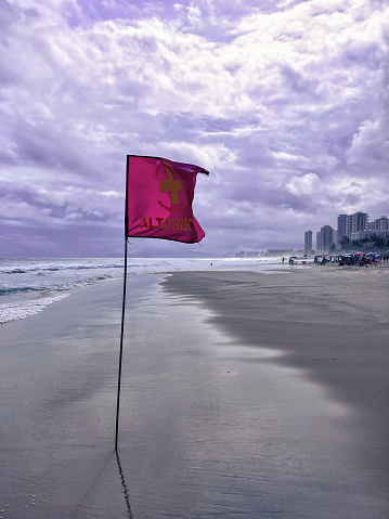 Flag on the beach indicating danger, landscape with many clouds. Taken by iPhone 13 Pro Max. Edited in Adobe lightroom and Adobe Photoshop.