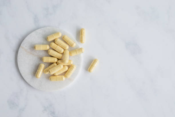 желтые капсулы добавки на белом мраморном фоне - anti aging pill capsule vitamin pill стоковые фото и изображения