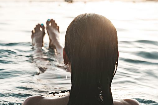 Over the shoulder view  of caucasian woman with long hair in sea at sundown