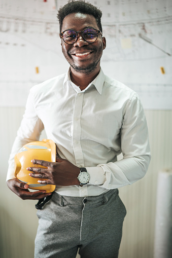 Young man african american engineer in an orange construction helmet stands with a project