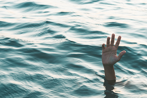 Hand of an unrecognizable person who is reaching for help and is drowning. Representing refugee deaths in the sea.