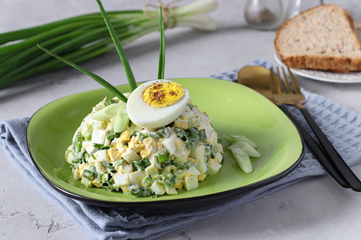 Salad with egg and green onions dressed with mayonnaise on plate on gray background