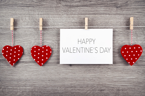 Greeting card and red hearts on clothesline against wooden background