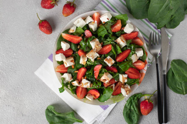 Healthy salad with strawberries, spinach, feta and pine nuts dressed with balsamic in plate on gray background stock photo