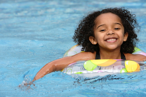Cute little girl wearing swim goggles enjoys a day in the backyard swimming pool