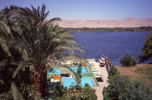 Idyllic scene as the calm waters of the River Nile reflect the buildings on the riverbank in the early morning sunshine. Luxor, Upper Egypt.