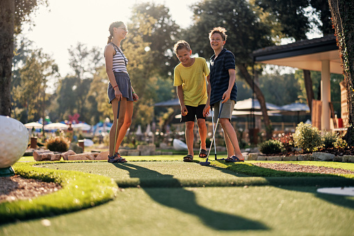 Three teenage kids having fun playing mini golf.