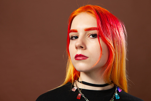 Close-up studio portrait of an 18 year old woman with brightly dyed hair on a brown background