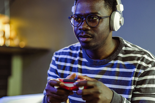Handsome African-American man playing video games while sitting on the sofa at home. He is concentrating and holding joystick