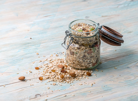 Jar full of oatmeal with raisins and nuts, some dried fruits open, some scattered